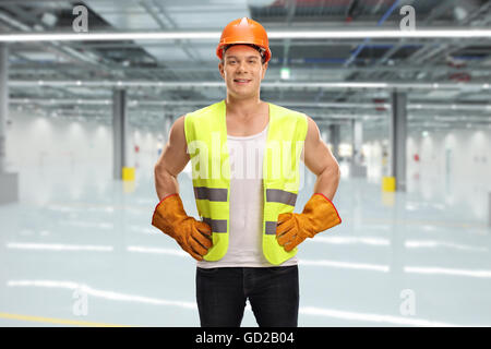 Cheerful male worker with an orange helmet and green reflective vest posing in a factory hall Stock Photo
