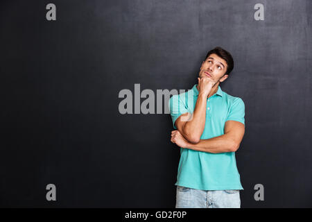Pensive young man standing and thinking over chalkboard background Stock Photo