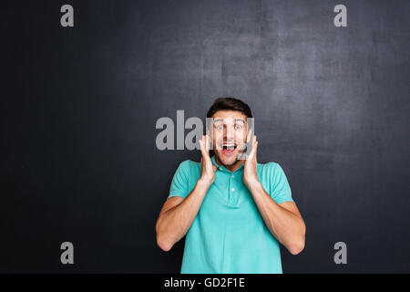 Cheerful surprised young man with mouth opened standing over chalkboard background Stock Photo
