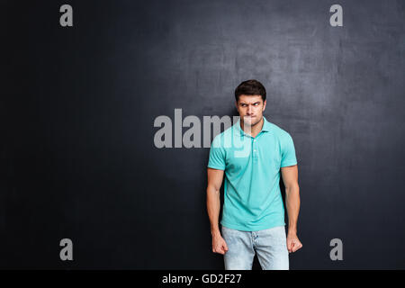 Angry irritated young man stnding and looking away over chalkboard background Stock Photo