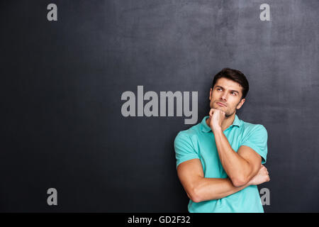 Thoughtful handsome young man standing and thinking over chalkboard background Stock Photo