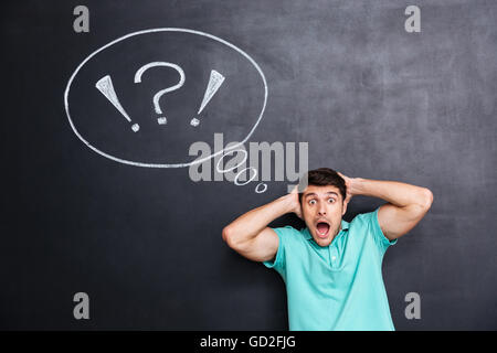 Shocked astonished young man over chalkboard background with blank speech bubble Stock Photo