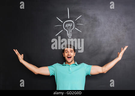 Smiling excited young man standing and having an idea over chalkboard background Stock Photo