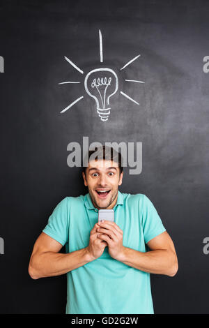 Cheerful excited young man holding smartphone and having an idea over chalkboard background Stock Photo