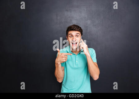 Happy excited young man talking on mobile phone and pointing on it over chalkboard background Stock Photo