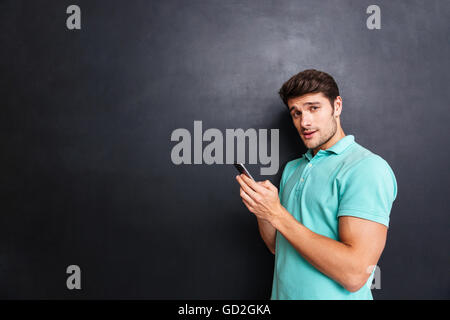 Confident handsome young man standing and using smartphone over blackboard background Stock Photo