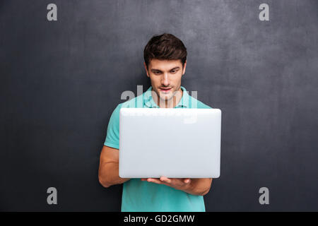 Concentrated handsome young man standing and using laptop over chalkboard background Stock Photo