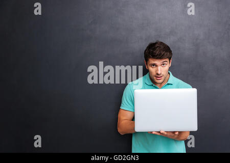 Thoughtful attractive young man using laptop over blackboard background Stock Photo