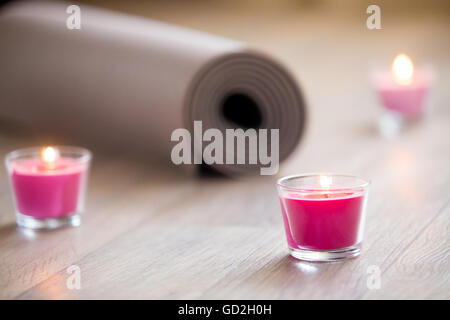 Rose-colored lighted pink candle and rolled brown yoga, pilates mat on the floor ready for workout. Close up. Healthy life Stock Photo