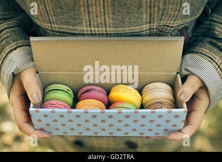 Woman wearing coat holding box with colorful French macaroons in her hands Stock Photo