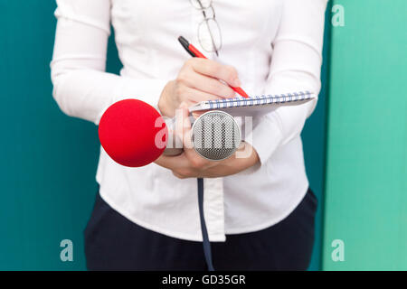 Female journalist or reporter at press conference, taking notes, holding microphones Stock Photo