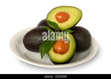 Fresh Healthy Whole and Halved Avocados Covered in Lemon Juice on White Round Plate with Basil Leaves in Clean White Background Stock Photo