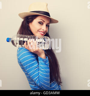 Happy fun young woman in hat holding bottle of pure water with natural emotional face. Toned closeup portrait Stock Photo