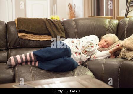 A grey haired woman lying on a sofa taking a nap. Stock Photo