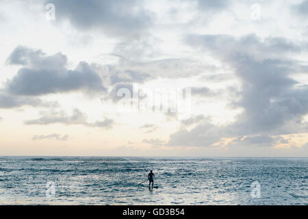 Man stand up paddling in calm waters at dusk Stock Photo