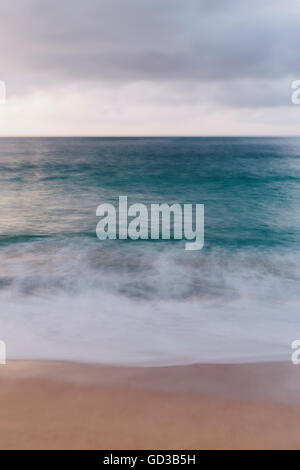 The ocean viewed from the beach, waves breaking on the beach and overcast sky. Stock Photo