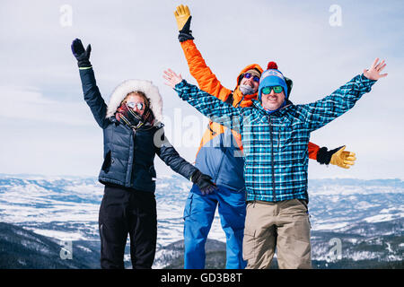 Three people, two men and a young woman standing on top of a mountain with arms outstretched. Stock Photo