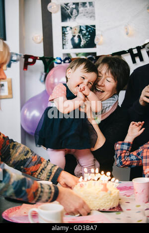 A family gathered to celebrate a one year old girl's birthday party. A cake with lots of candles. Stock Photo