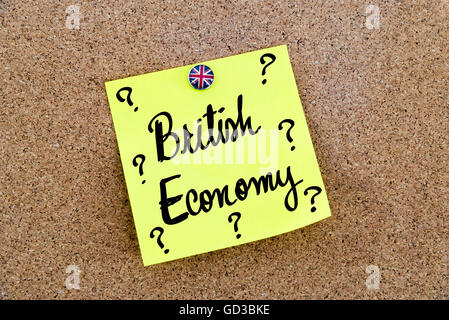 Yellow paper note pinned on cork board with Great Britain flag thumbtack, written text BRITISH ECONOMY and question marks, United Kingdom exit from European Union Stock Photo