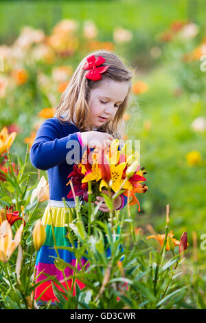 Cute little girl picking lily flowers in blooming summer garden. Child holding lilies bouquet in beautiful flower field. Stock Photo