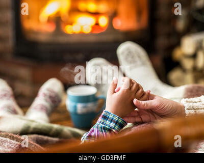 Warming and relaxing near fireplace. Mother and daughter holding hands in front of fire. Stock Photo