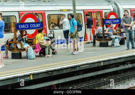 Passengers sit on benches at Earl's Court London Underground Station while waiting for their train. Stock Photo