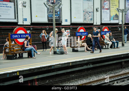 Passengers sit on benches at Earl's Court London Underground Station while waiting for their train. Stock Photo