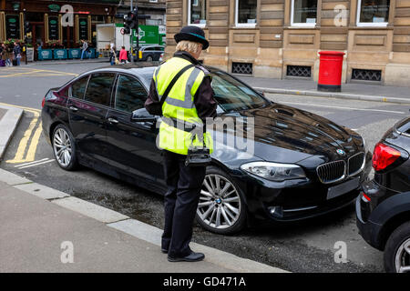 Traffic warden issuing a parking ticket to a BMW saloon car parked illegally, Queen Street, Glasgow, Scotland, UK Stock Photo