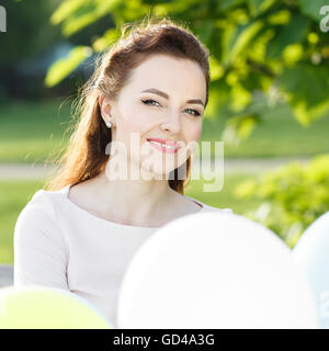 Young happy woman with bunch of balloons in summer park. Beautiful girl in dress at summer time Stock Photo