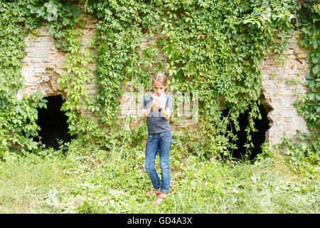 Small teenage girl standing with notebook near old brick ruins overgrown with wild grapevine. Summer italian vacation background Stock Photo