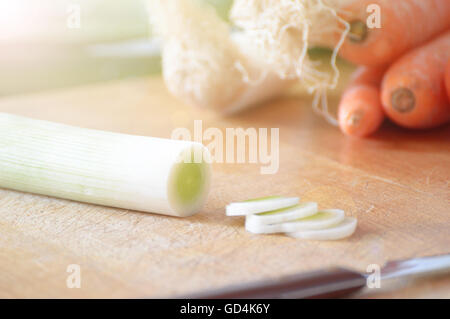 Cutting some leeks on a wooden table while cooking in a rustic kitchen. Stock Photo