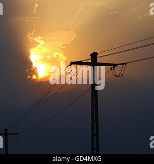 High voltage power lines in front of sun setting behind storm clouds Stock Photo