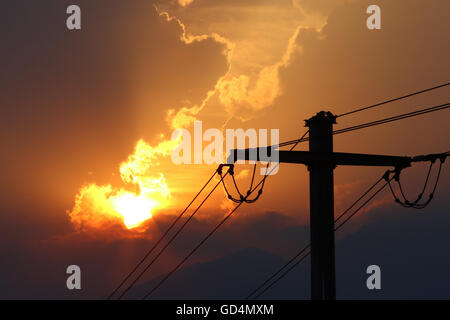 High voltage power lines in front of sun setting behind storm clouds Stock Photo
