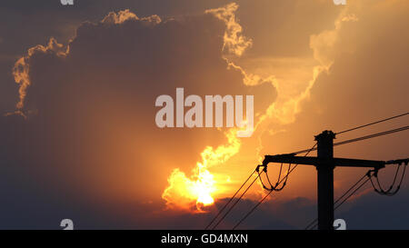 High voltage power lines in front of sun setting behind storm clouds Stock Photo