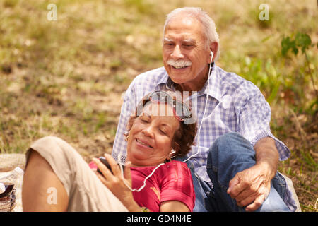 Old people, senior couple, elderly man and woman in park. Grandpa and grandma listening to song, music with mp3 player Stock Photo