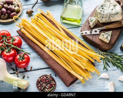 Pasta ingredients. Cherry-tomatoes, spaghetti pasta, rosemary and spices on the wooden table. Stock Photo