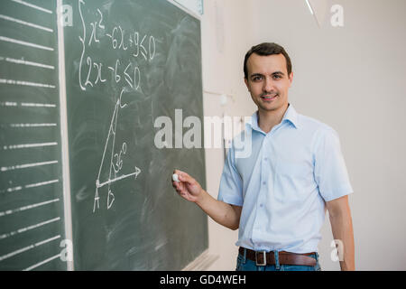 Young male teacher or student holding chalk writing on chalkboard in classroom Stock Photo