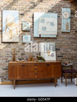 Retro sideboard in hallway with exposed brick walls and assorted artworks by Jo Oakely Stock Photo