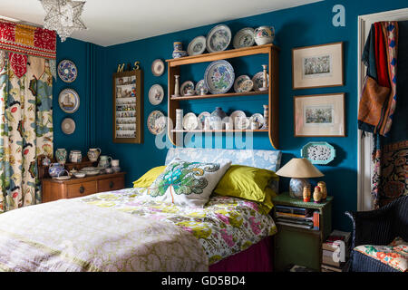 Poole pottery displayed on wooden shelf in bedroom painted in Deep Space Blue by Little Greene.The bed is upholstered and covere Stock Photo