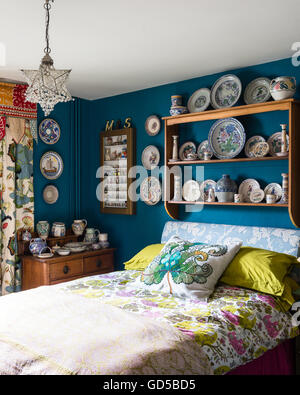 Poole pottery displayed on wooden shelf in bedroom painted in Deep Space Blue by Little Greene.The bed is upholstered and cover Stock Photo