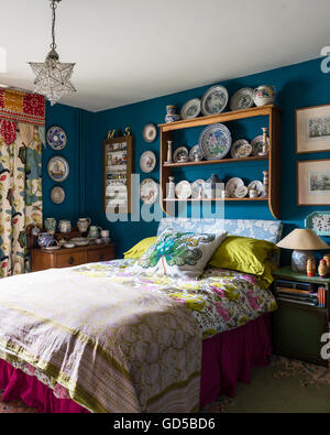 Poole pottery displayed on wooden shelf in bedroom painted in Deep Space Blue by Little Greene.The bed is upholstered and cover Stock Photo