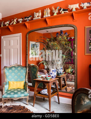 A collection of Staffordshire figures along high shelf in room with winged back armchair and vase of peacock feathers. Stock Photo