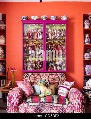 Club sofa upholstered in kilim material beneath glass-fronted pink cabinet containing collection of marionette puppets. Stock Photo