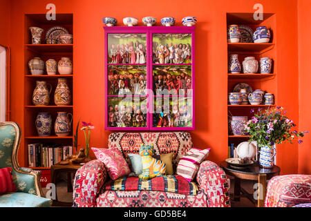 Club sofa upholstered in kilim material beneath glass-fronted pink cabinet containing collection of marionette puppets. Stock Photo