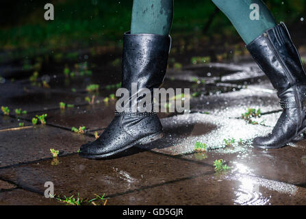 Female legs in black leather high boots on cobble  the edge of rain puddle, closeup. Concept  protection against rainy weather, waterproof footwear Stock Photo