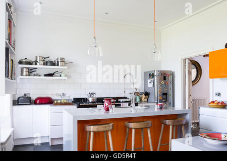 Wooden bar stools in high ceilinged kitchen with white metro tiles. The clear glass dome lights are from Baileys Home Stock Photo