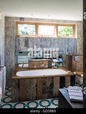 Bath tub clad in recycled floorboards in bathroom with Parquet Turquoise vinyl floor tiles by Neisha Crosland Stock Photo