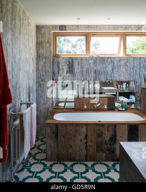 Bath tub clad in recycled floorboards in bathroom with Parquet Turquoise vinyl floor tiles by Neisha Crosland Stock Photo
