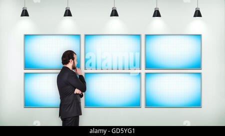 Businessman looking on blank six  tv screen on concrete wall in loft room Stock Photo