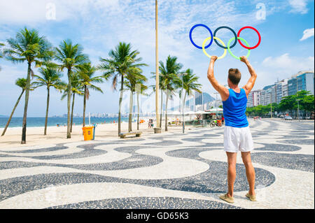 RIO DE JANEIRO - MARCH 10, 2016: Athlete stands with Olympic rings on the iconic wave pattern of the Copacabana Beach sidewalk. Stock Photo